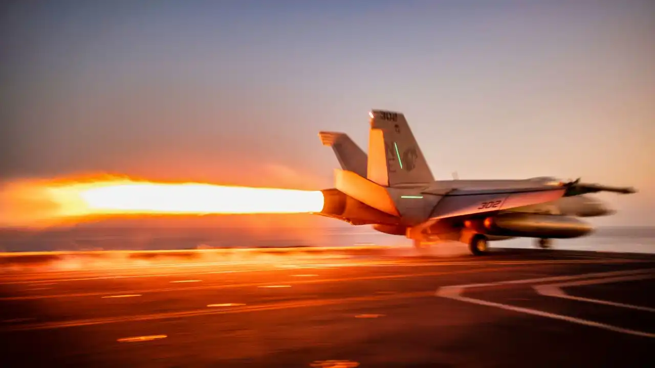 Block III F/A-18E Super Hornet launching from carrier at dusk
