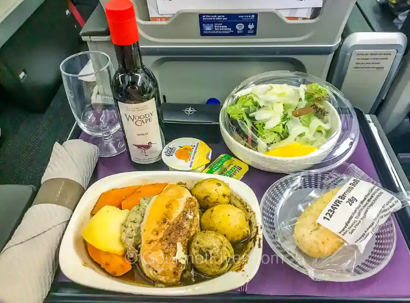 plated meal service with wine glass and cutlery in premium economy cabin